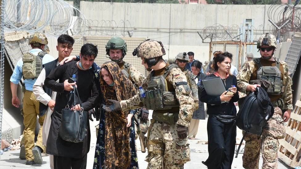 Soldiers help a woman, who fell due to high temperature at the Kabul International Airport as thousands of Afghans rush to flee the Afghan capital of Kabul