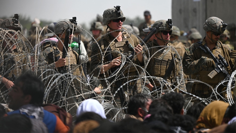 US soldiers stand guard behind barbed wire as Afghans sit on a roadside near the military part of the airport in Kabul on 20 August 2021