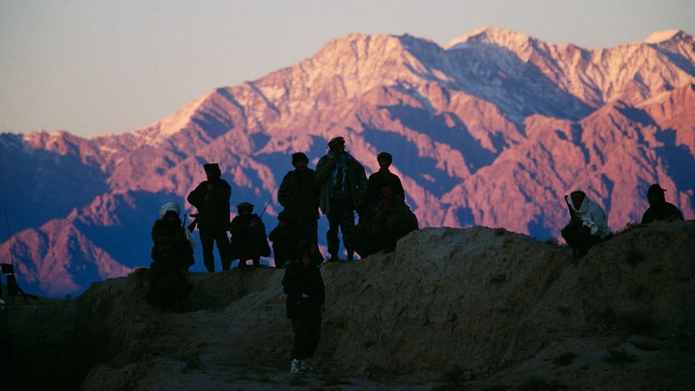 A group of soldiers are silhouetted against a mountain backdrop