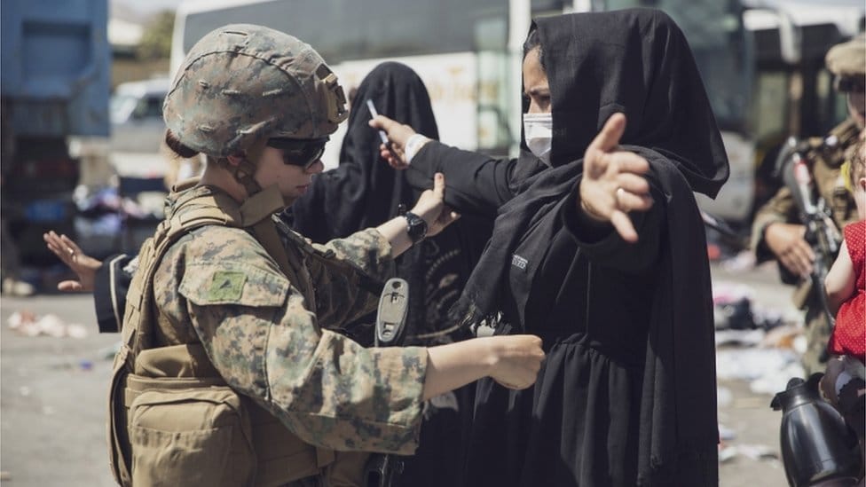 A U.S. Marine checks a woman as she goes through the Evacuation Control Center (ECC) during an evacuation at Hamid Karzai International Airport