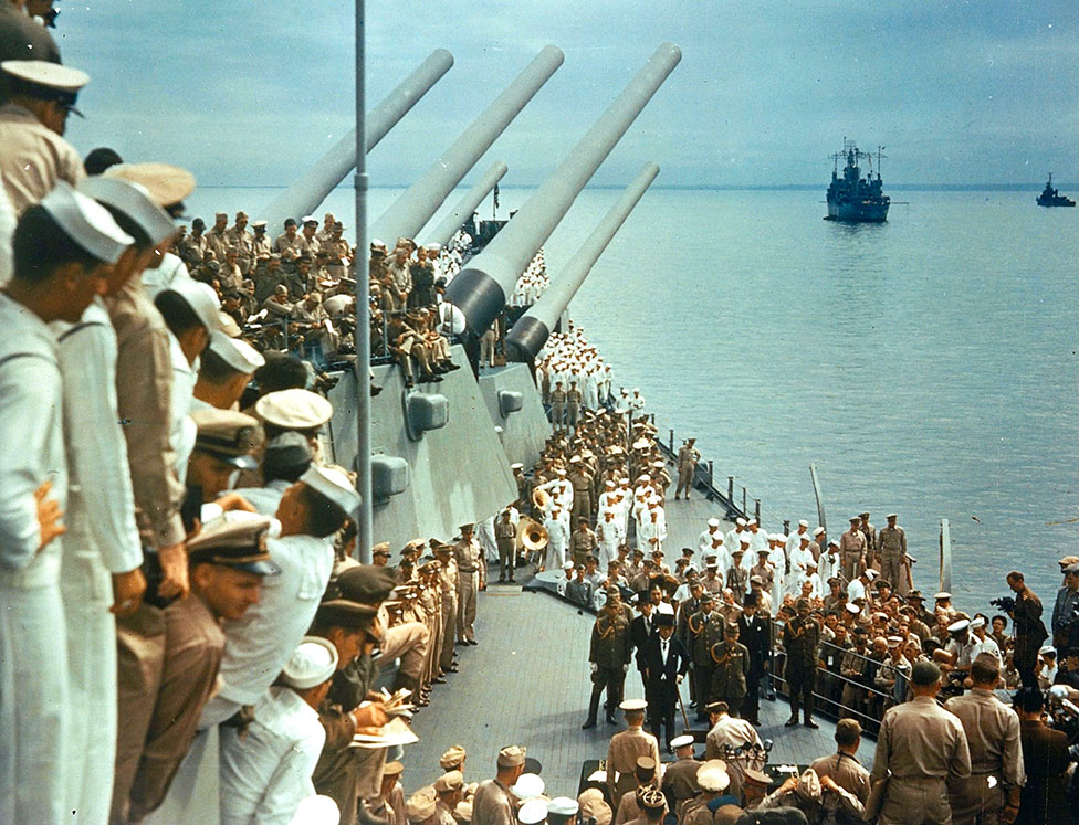 Soldiers and sailors on the decks of the USS Missouri watch representatives from Japan formally surrender