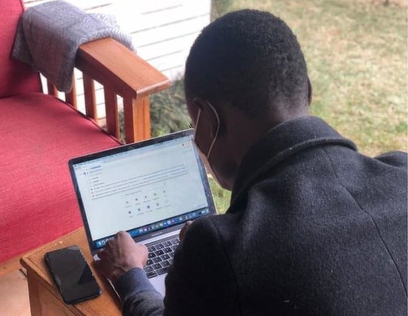 David, a Kenyan academic writer with a mask working on a laptop.