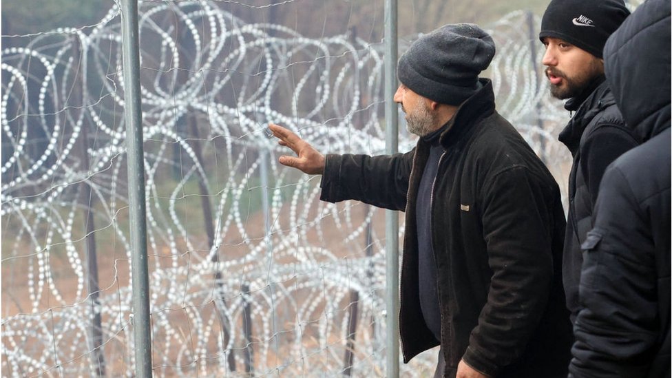 Belorusija, Poljska i migrantska kriza: Kako su hiljade ljudi završile zaglavljene na istočnoevropskoj granici 5 Migrants stand next to a razorwire fence on the Belarus-Poland border