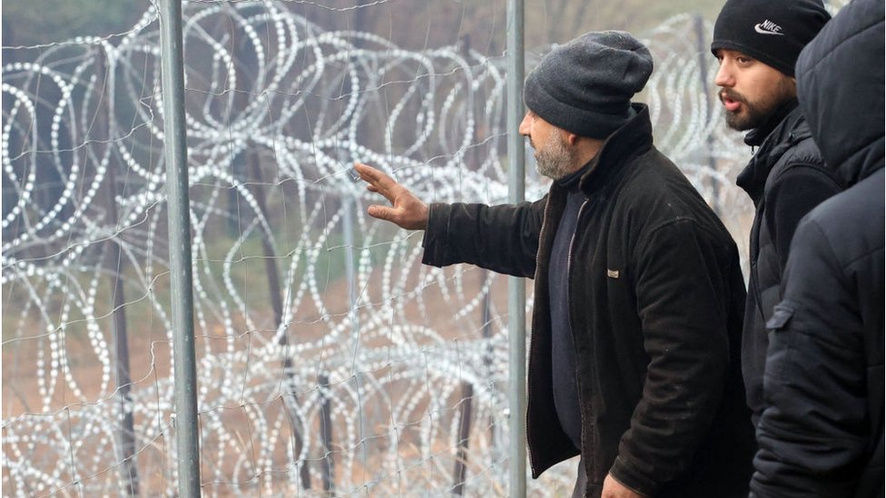 Migrants stand next to a razorwire fence on the Belarus-Poland border