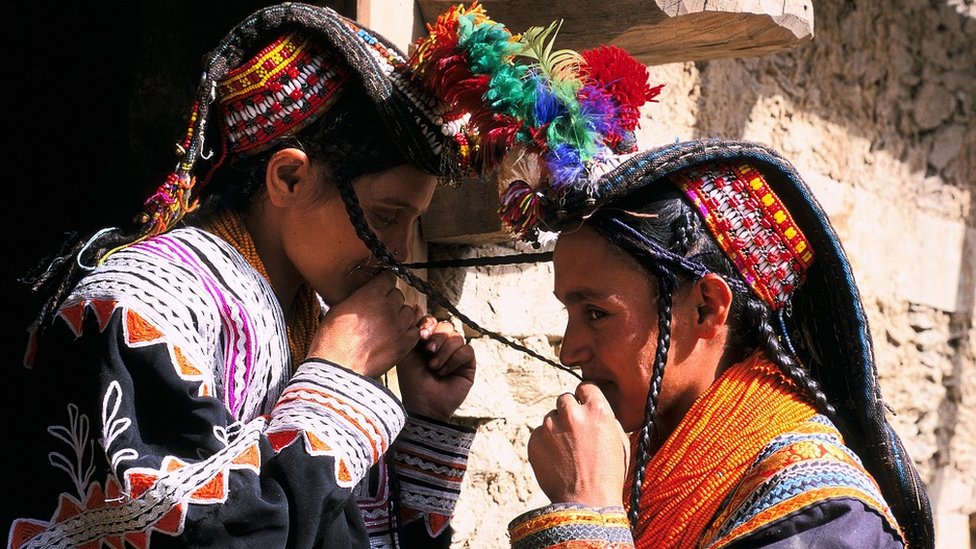 Kalash young girls, dressed in traditional attire, kiss each other's plats, as per tradition