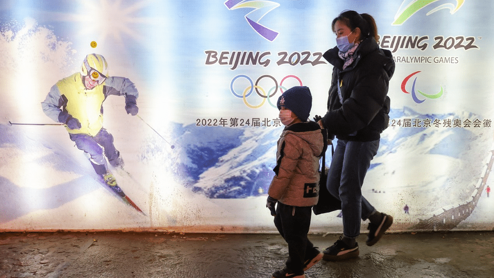 Woman and child walk past a poster for the Beijing Winter Olympics