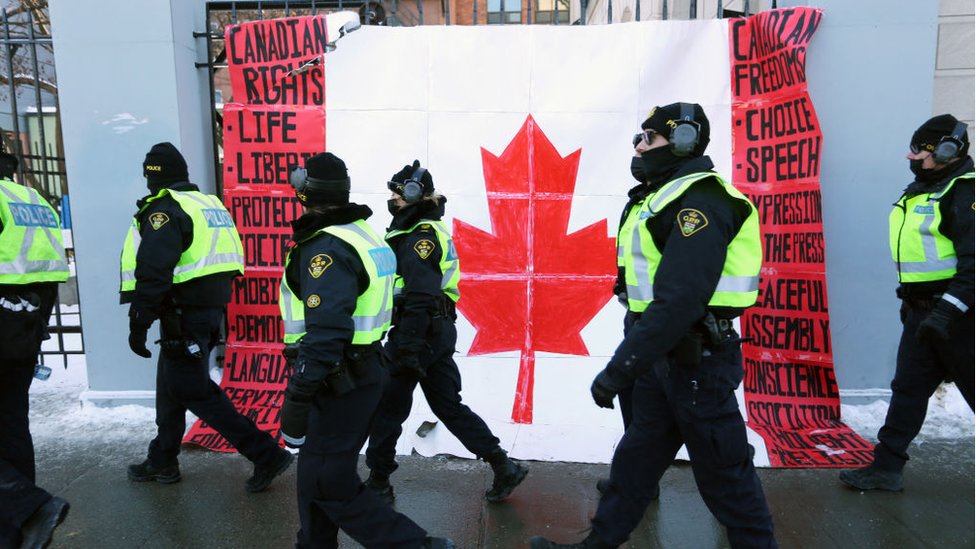 Korona virus i protesti: Policija u Kanadi rasterala demonstrante sa graničnog mosta, u Otavi i dalje vanredno stanje 7 A group of police officers walk past a Canadian flag near Parliament Hill
