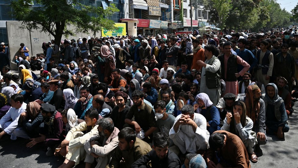 Ukrajina i Rusija: „Pobegla sam iz Kabula, a sada sam usred rata u Kijevu“ 6 People sitting outside a bank waiting to withdraw money in Kabul in September 2021