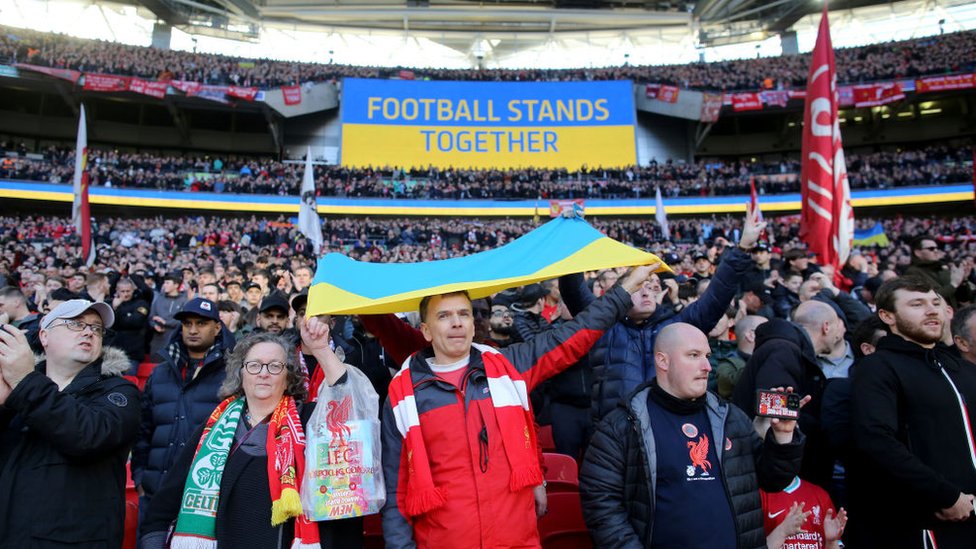Ukrajina i Rusija: Kako sportski svet reaguje na rat u Ukrajini 1 Liverpool fans display a Ukraine flag as the big screen reads 'Football Stands Together' before the Carabao Cup Final match between Chelsea and Liverpool at Wembley Stadium on February 27