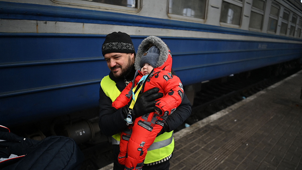 A volunteer holds a baby to help him to get on board to a train which prepares to depart from a station in Lviv, western Ukraine, enroute to Poland, on March 3, 2022