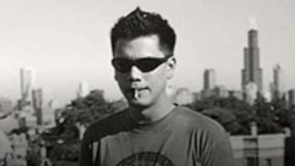 Tom Justice standing in front of the Chicago skyline with a cigarette in his mouth