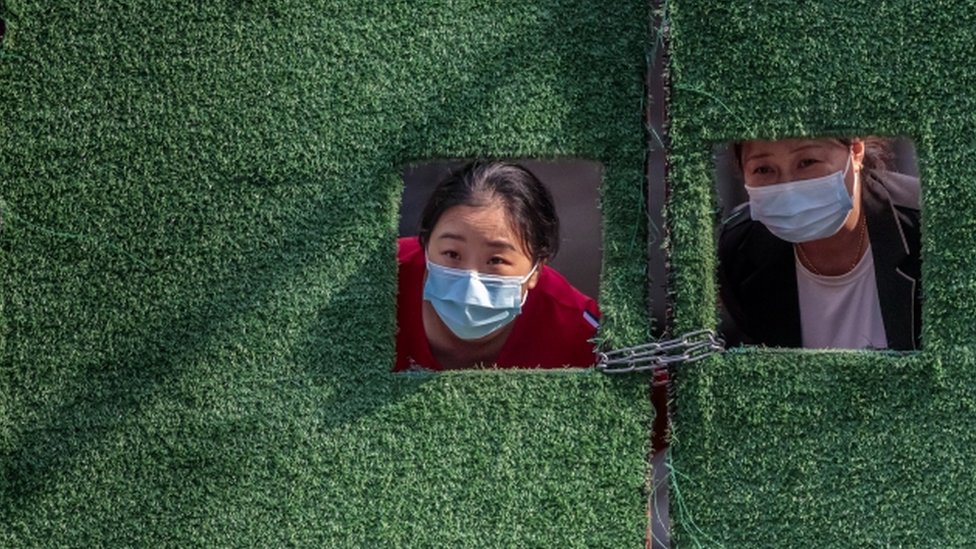 Women in quarantine look through small windows in a green fence, amid the Covid-19 lockdown in Shanghai, on 2 May 2022