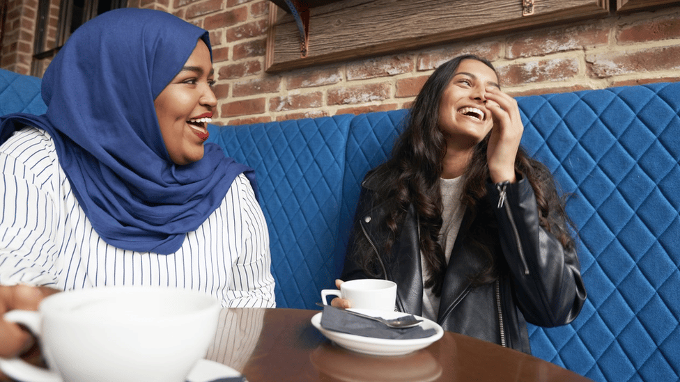 Two young female friends sharing a laugh in a cafe