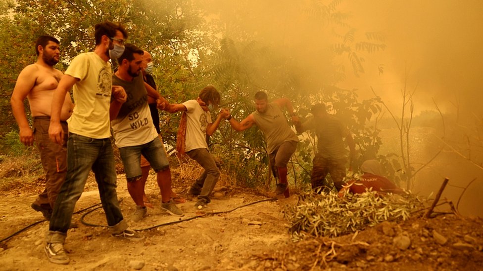 A man holding a hose is helped to climb a slope, as a wildfire burns in the village of Gouves, on the island of Evia, Greece, August 8, 2021
