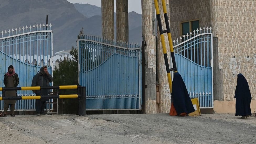 Women wearing a burqa walk toward the main gate of Laghman University as Taliban fighters stand guard in Mihtarlam, Laghman province