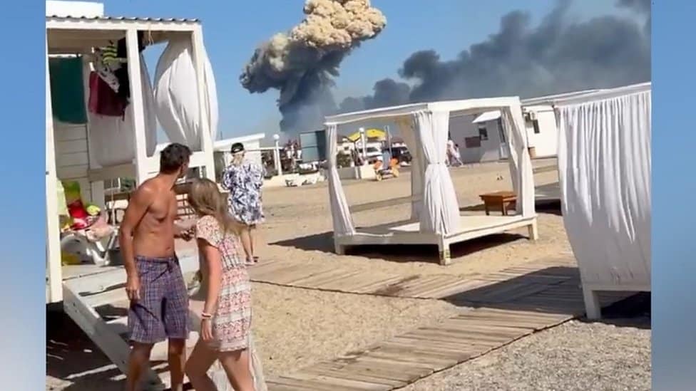 Rusija i Ukrajina: Eksplozije u ruskoj vojnoj bazi na Krimu, Zelenski poručuje da „rat mora da se završi oslobođenjem poluostrva" 1 People on beach in Crimea, plume of smoke in background