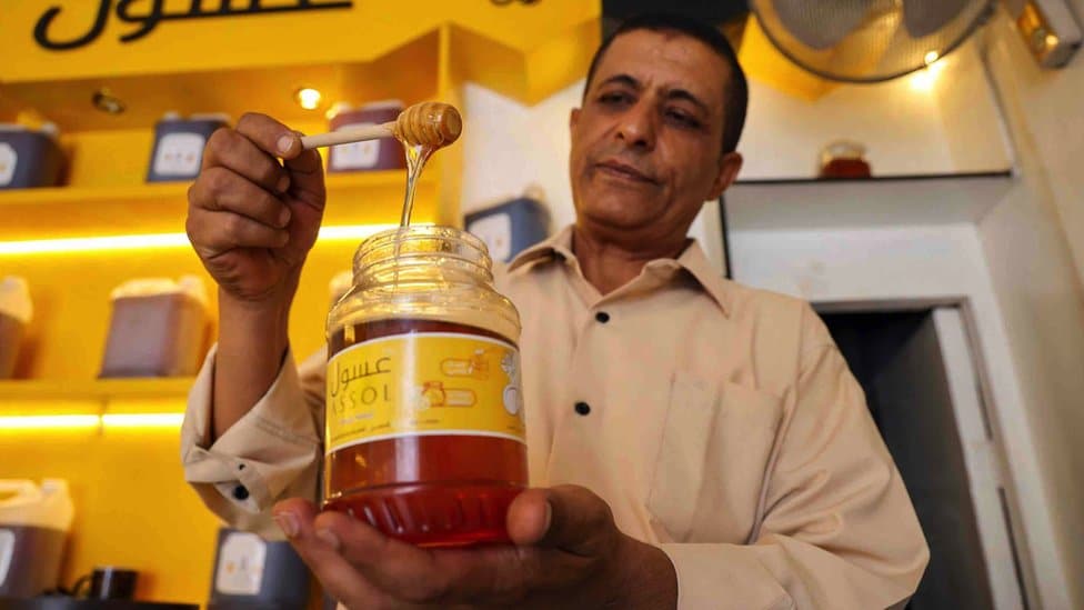 A Yemeni vendor scoops honey from a jar at his shop in Yemen's third city of Taez in June 2022s. The United Nations says honey plays a "vital role" in Yemen's economy, with 100,000 households dependent on it for their livelihoods.