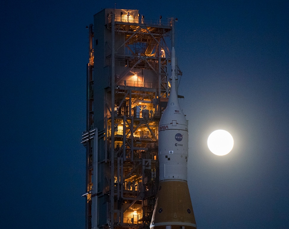 SLS-Orion at the launch pad with the Moon glowing in the sky and illuminating the area