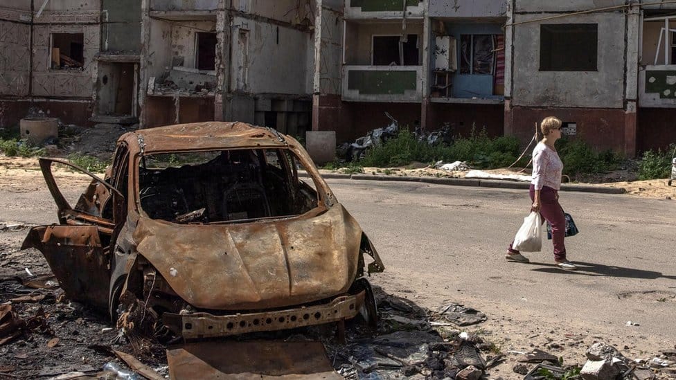 A woman walks past a burnt car and damaged residential building in Chernihiv, northern Ukraine, 22 August 2022