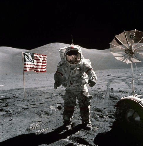 Apollo 17 Astronaut standing upon the lunar surface with the United States flag and a radio dish in the background