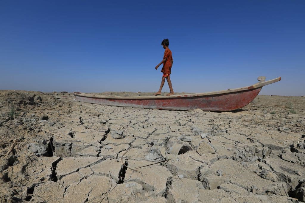 A boy walks on a boat left lying on the dried-up bed of a section of Iraq's receding southern marshes of Chibayish in Dhi Qar province, on June 28, 2022. - Iraq's drought reflects a decline in the level of waterways due to the lack of rain and lower flows from upstream neighboring countries Iran and Turkey.