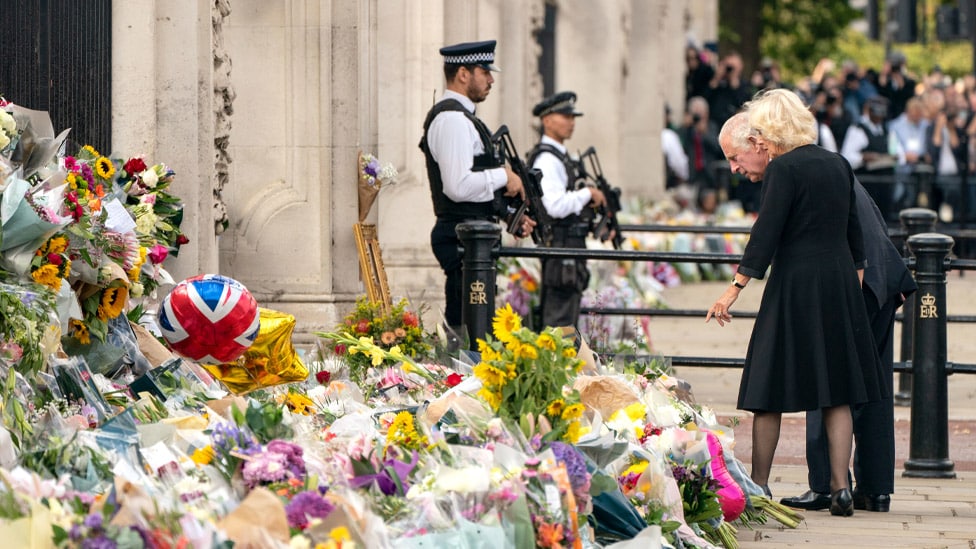 King Charles and Queen Camilla look at flowers outside Buckingham Palace