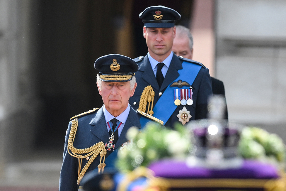 King Charles III and Prince William, Prince of Wales walk behind the coffin of Queen Elizabeth II during a procession from Buckingham Palace to the Palace of Westminster