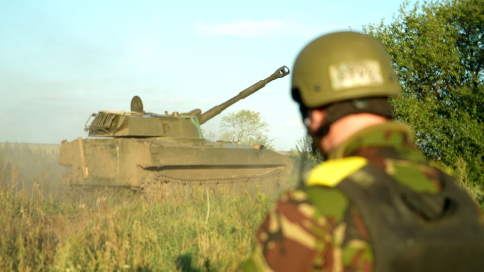A Ukrainian solider standing near an old Soviet self-propelled howitzer called “Gvozdika”