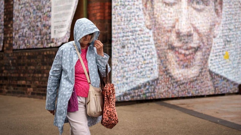 Cene, troškovi života i privreda: MMF upozorava na pad svetske ekonomije naredne godine 1 Woman walking in rain in front of street art.