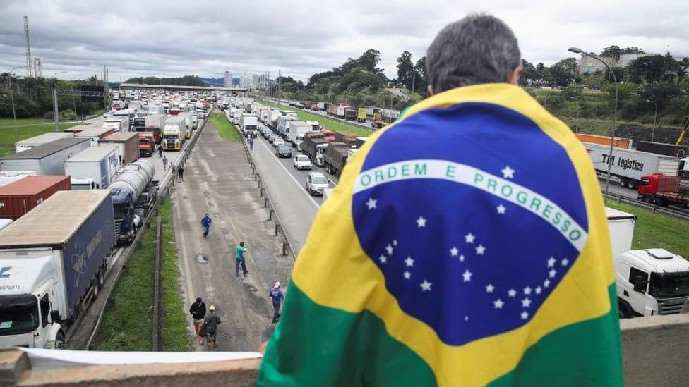 A man draped in a Brazilian flag looks on as supporters of Brazil's President Jair Bolsonaro, mainly truck drivers, block the Castello Branco highway during a protest over Bolsonaro's defeat in the presidential run-off election, in Barueri, Brazil November 1, 2022.