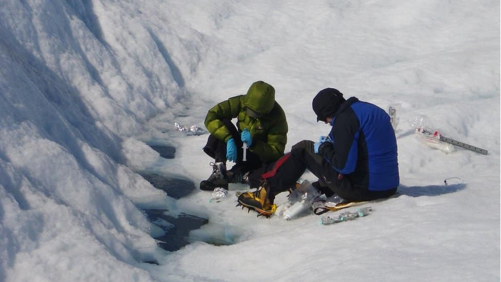 Klimatske promene: Iz otopljenih glečera možda prete tone bakterija 1 Dr Arwyn Edwards and Joseph Cook sampling glacier 'weathering crust' meltwater and ice to measure microbe numbers.