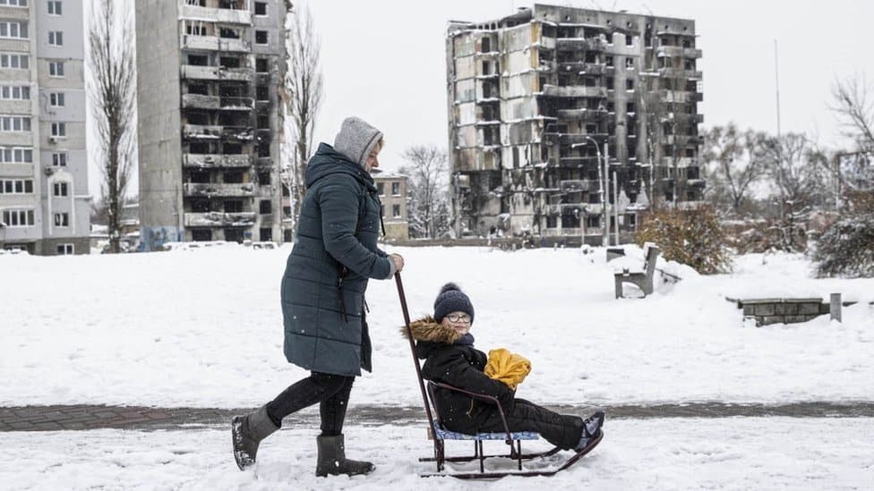 A woman carries the child after the snowfall as daily life continues in Borodianka