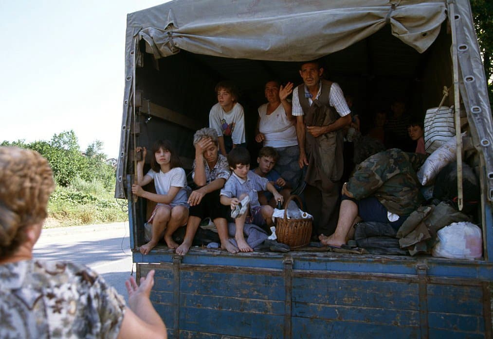 An extended Bosnian refugee family waves good-bye to a relative as they flee the riots in Mostar in a cargo vehicle, July 29, 1992