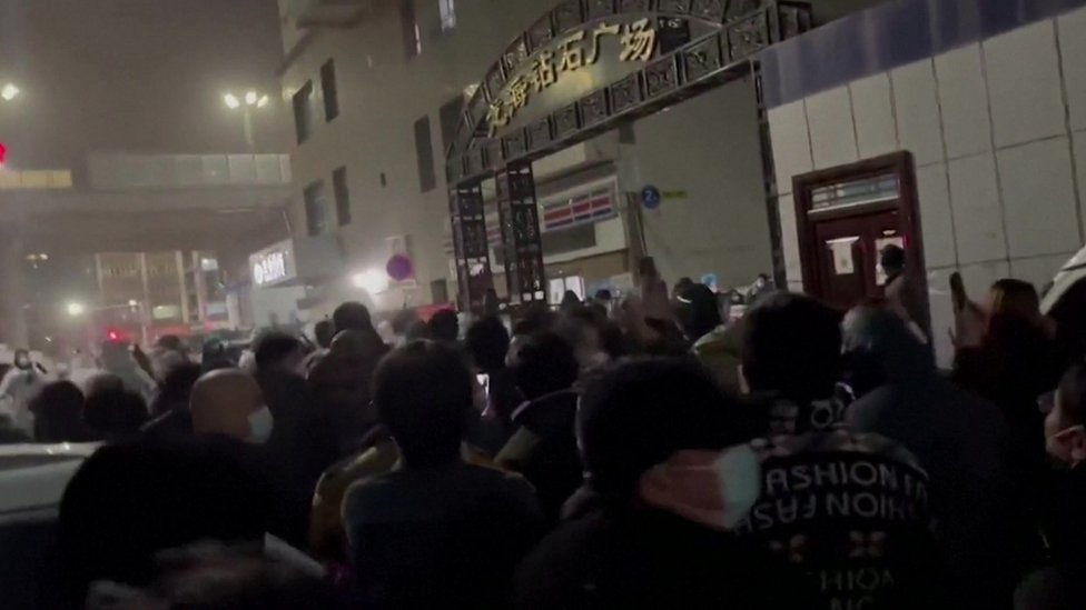 A crowd of dozens of people marches through the streets of Urumqi at night