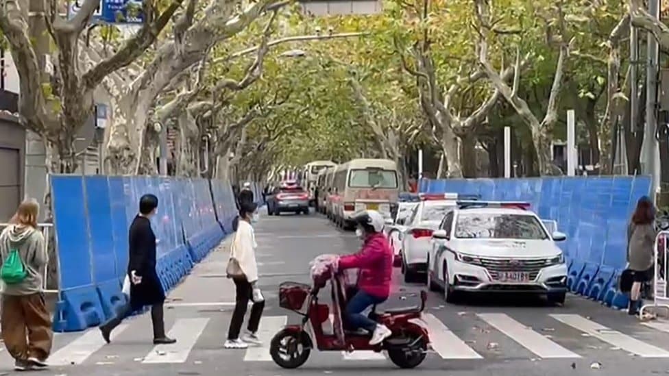 people walking past barricades and police presence on Wulumuqi street, named for Urumqi in Mandarin, in Shanghai on November 28, 2022