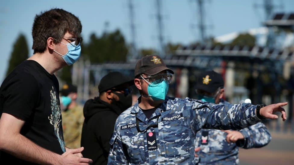 Pripadnik australijskih vazduhoplovnih snaga stoji pored čoveka koji nosi masku za lice