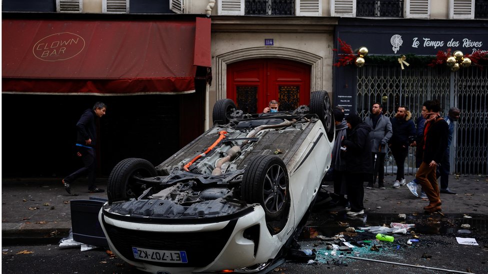 Francuska: Nasilni protesti u Parizu posle smrtonosnog napada na Kurde 3 People stand behind an overturned car in central Paris