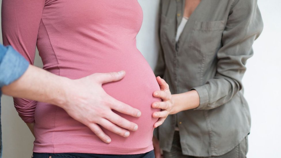 A couple with hands on their surrogate's baby bump