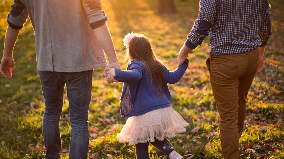 A child walking with a gay couple and holding hands