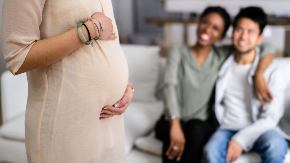 A couple looking at a surrogate mother who's touching her baby bump