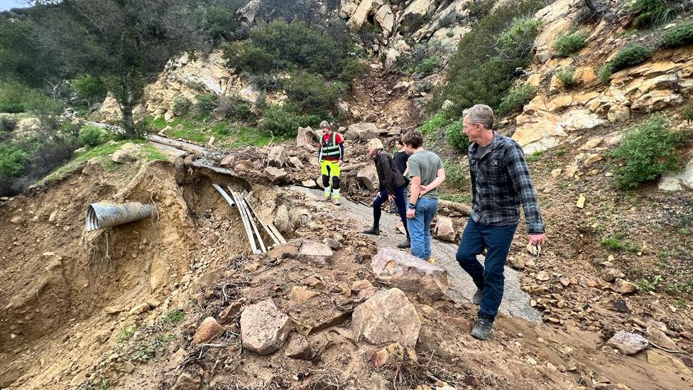 People trying to clear a road damaged by storms in California