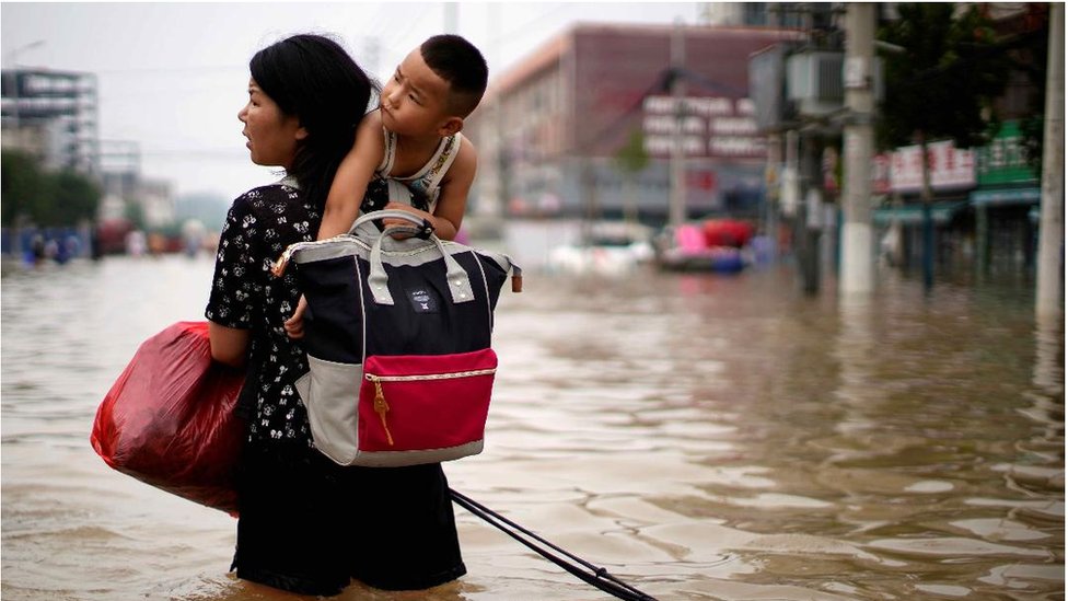 A woman carrying a child and belongings wades through floodwaters following heavy rainfall in Zhengzhou, Henan province, China July 23, 2021