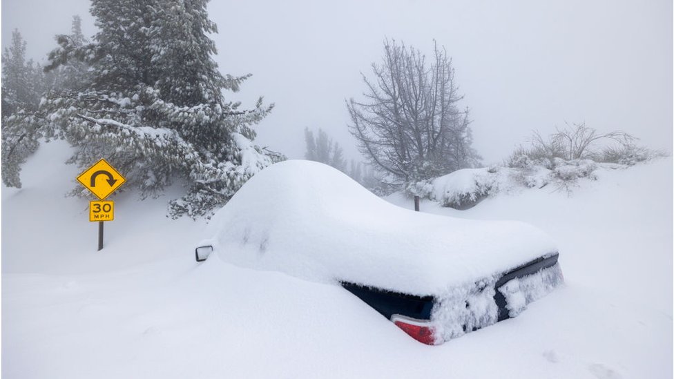 A vehicle buried under snow is abandoned along a highway