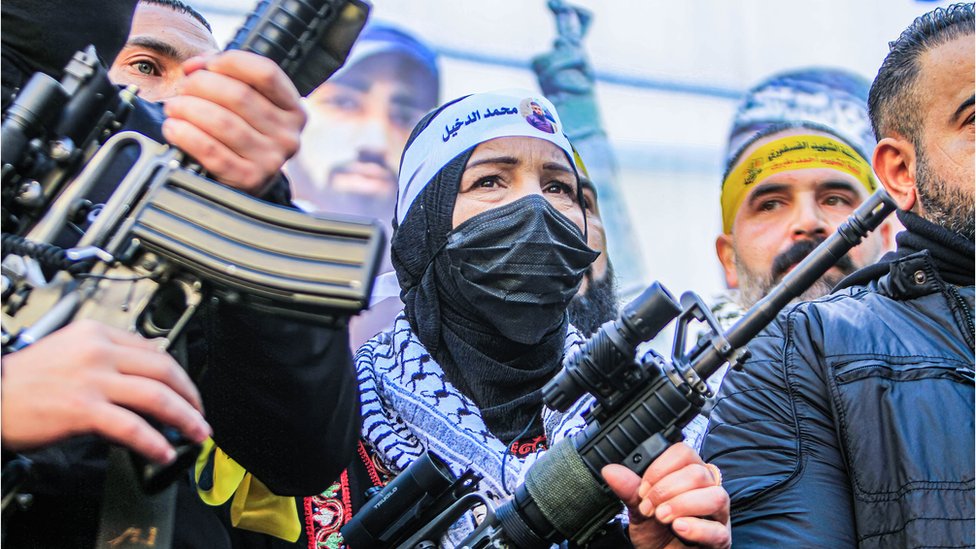 The mother of one of the Palestinians who was shot dead by the Israeli forces holds a weapon, and next to her are armed men, some of them from the Lions' Den