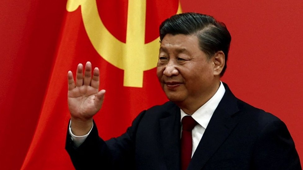 Chinese president Xi Jinping waving in front of a Chinese flag