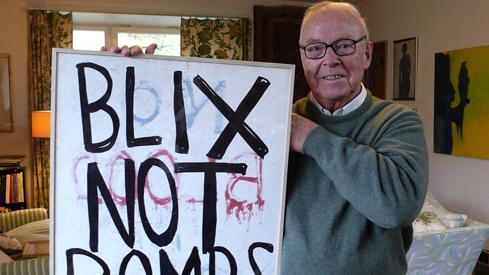 Hans Blix in 2013 holding a framed placard saying "Blix not Bombs"
