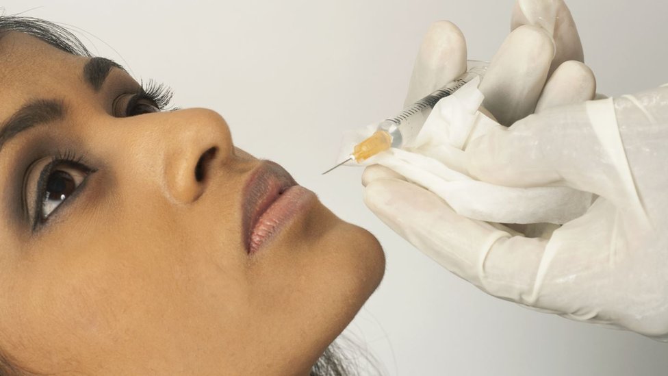 Doctor injecting collagen into young woman's lip