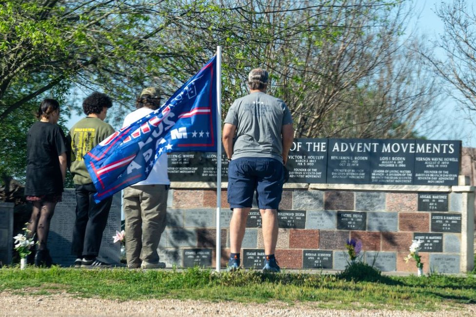People stand with heads bowed before a monument to the dead at Waco