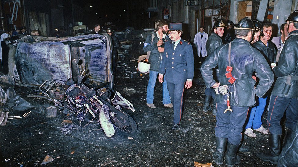 A picture taken on October 3, 1980 shows firemen standing by the wreckage of a car and motorcycle after a bomb attack at a Paris synagogue rue Copernic killing four people