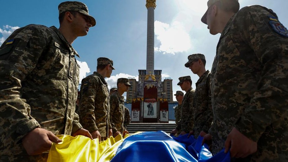 Rusija i Ukrajina: Češkoj učiteljici preti zatvor zbog „širenja ruske propagande" na časovima 1 Ukrainian troops hold a Ukrainian flag over a coffin of a serviceman